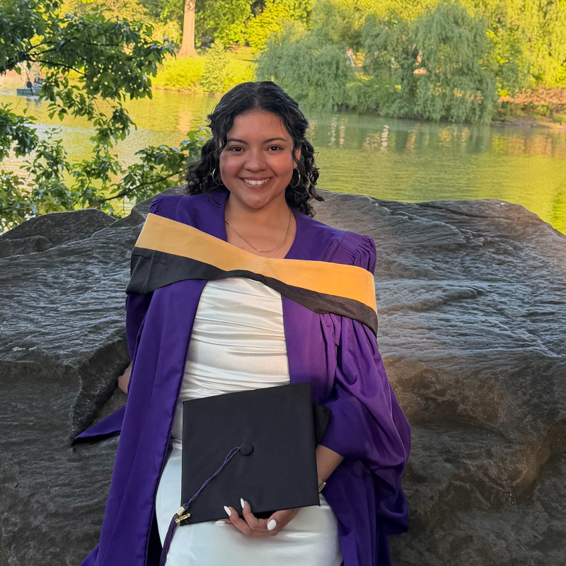 Women standing against nature in her graduation gown.