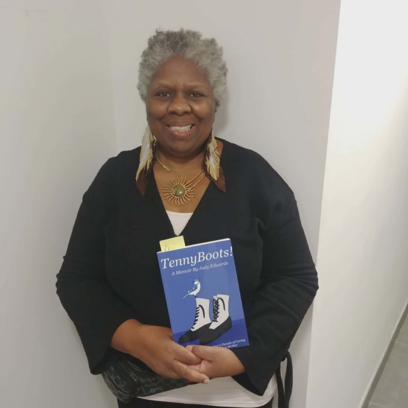 Woman posing against a blank wall holding a blue book.