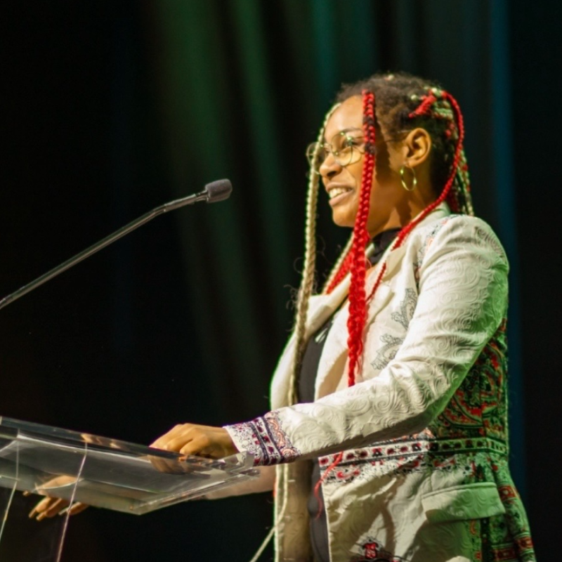 Woman standing if front of a microphone speaking.