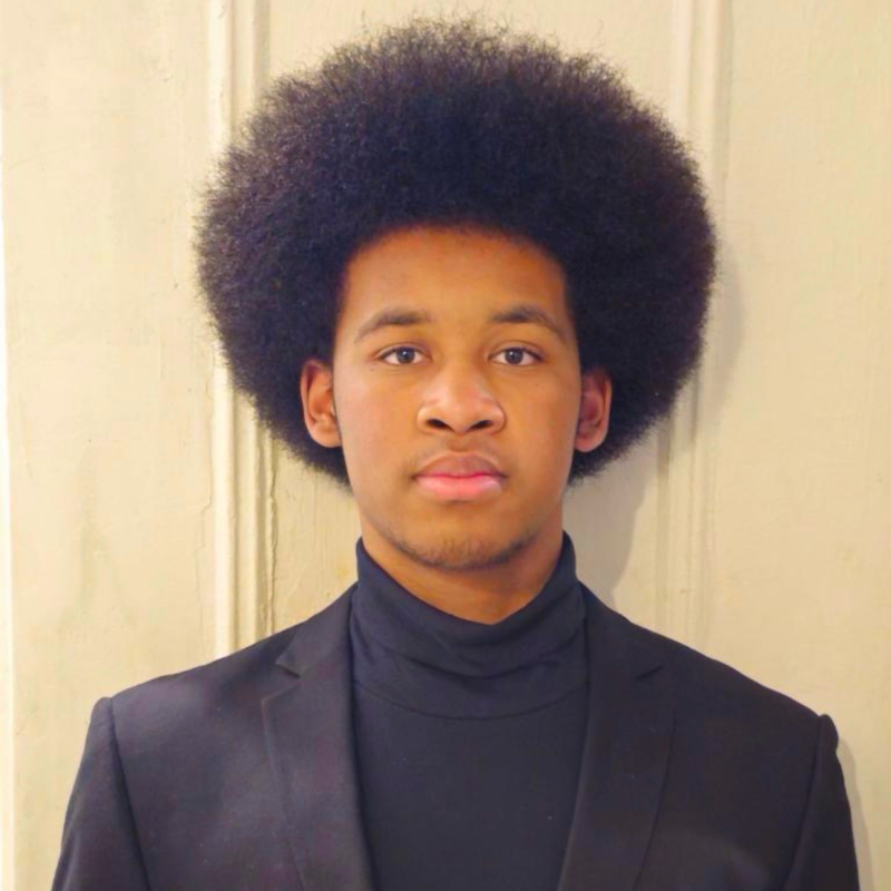 Man posing against a light color wall in all black.
