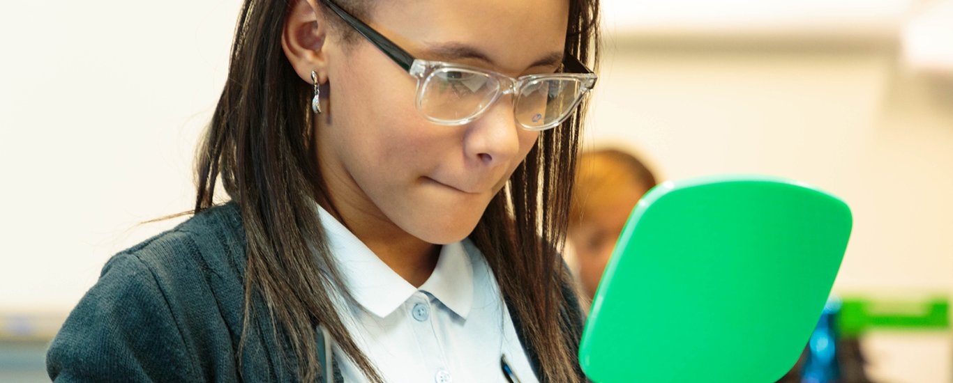 Young girl looks at herself in mirror wearing new glasses