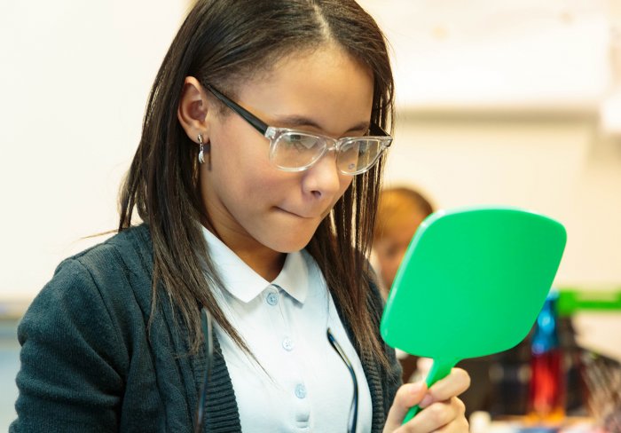 Young girl looks at herself in mirror wearing new glasses