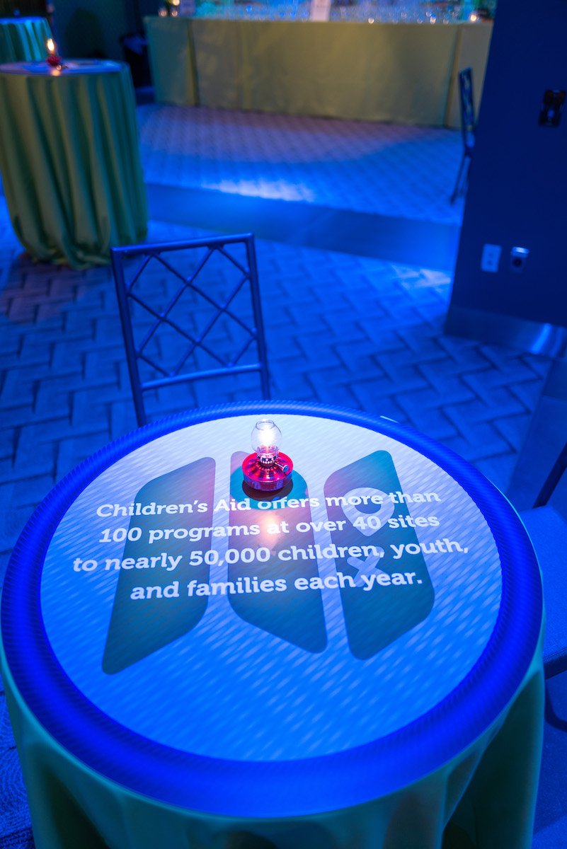 Cocktail tables topped with "badges of honor" by way of Children's Aid facts.