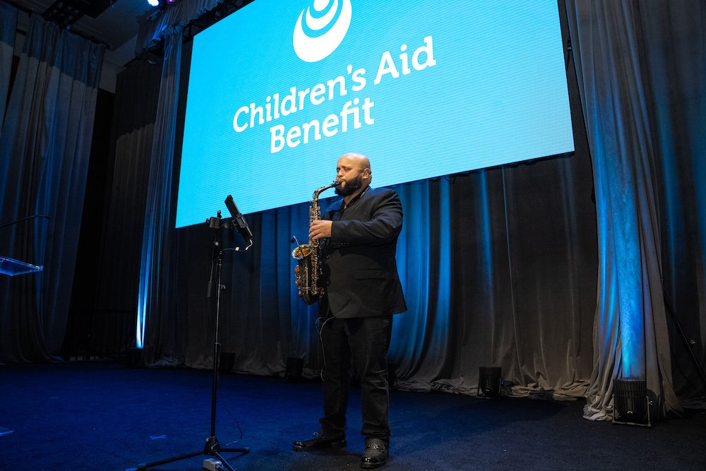 Children's Aid alumnus Donny Mendez entertaining the in-person audience with his musical stylings on the saxophone